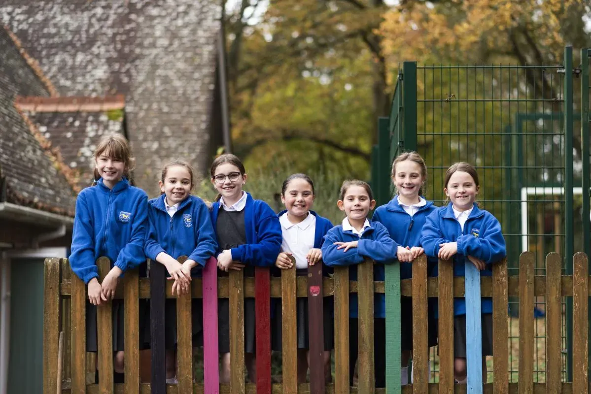 A group of pupils in blue fleeces smiling over a colourful wooden fence