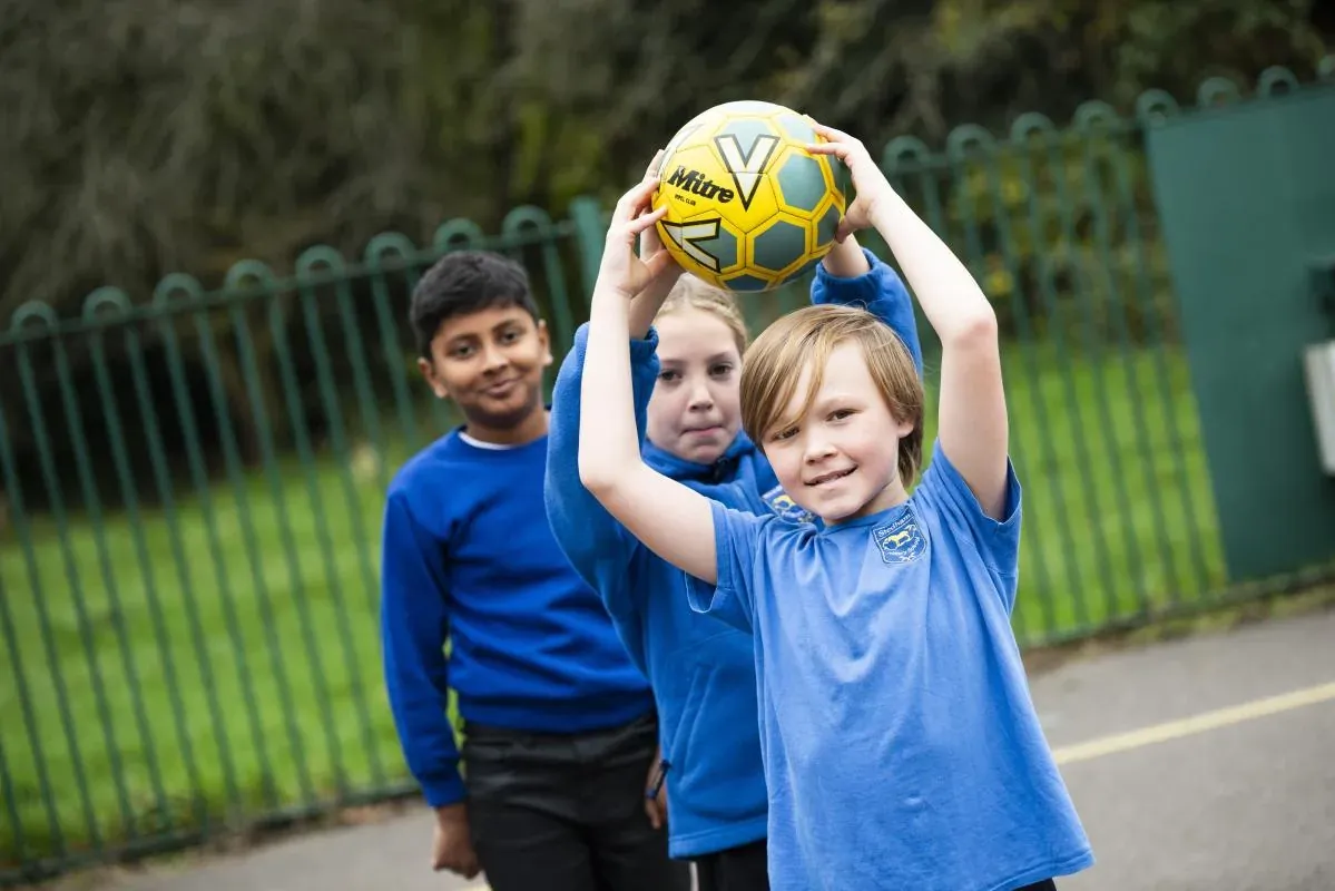Three smiling pupils in blue school tops holding a football aloft