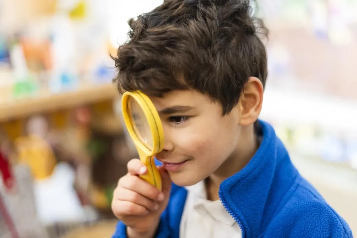 A boy in a blue fleece looking through a magnifying glass