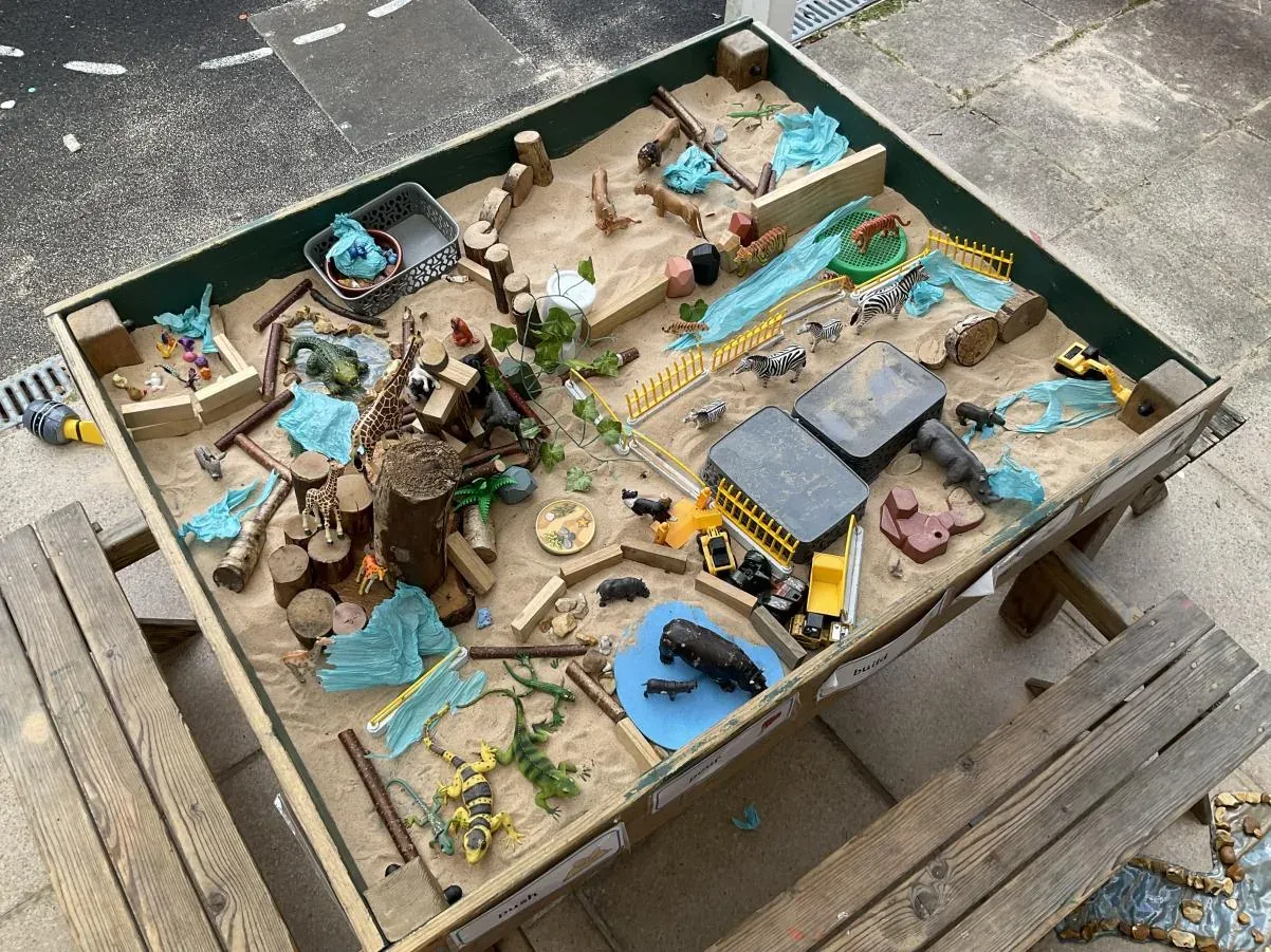 An outdoor small-world tray of sand, water, animals and diggers set out for the children