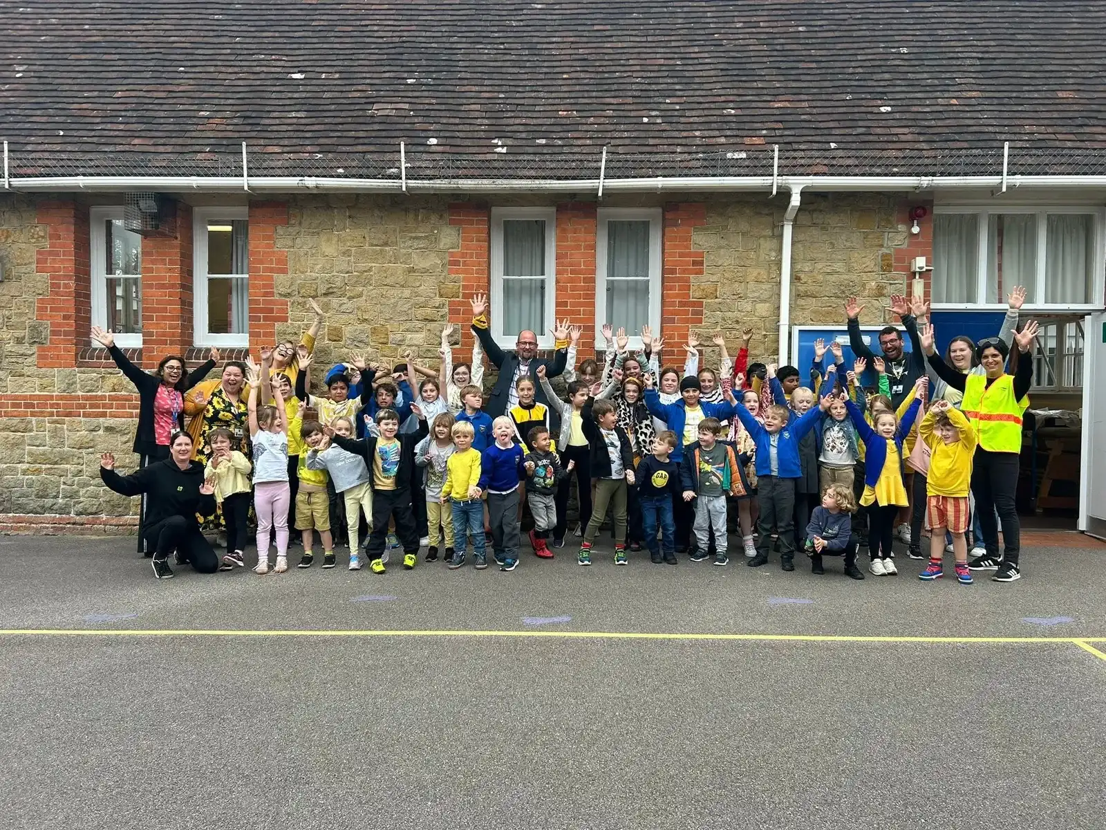 The whole school, children and staff, waving together in the playground in front of the school building
