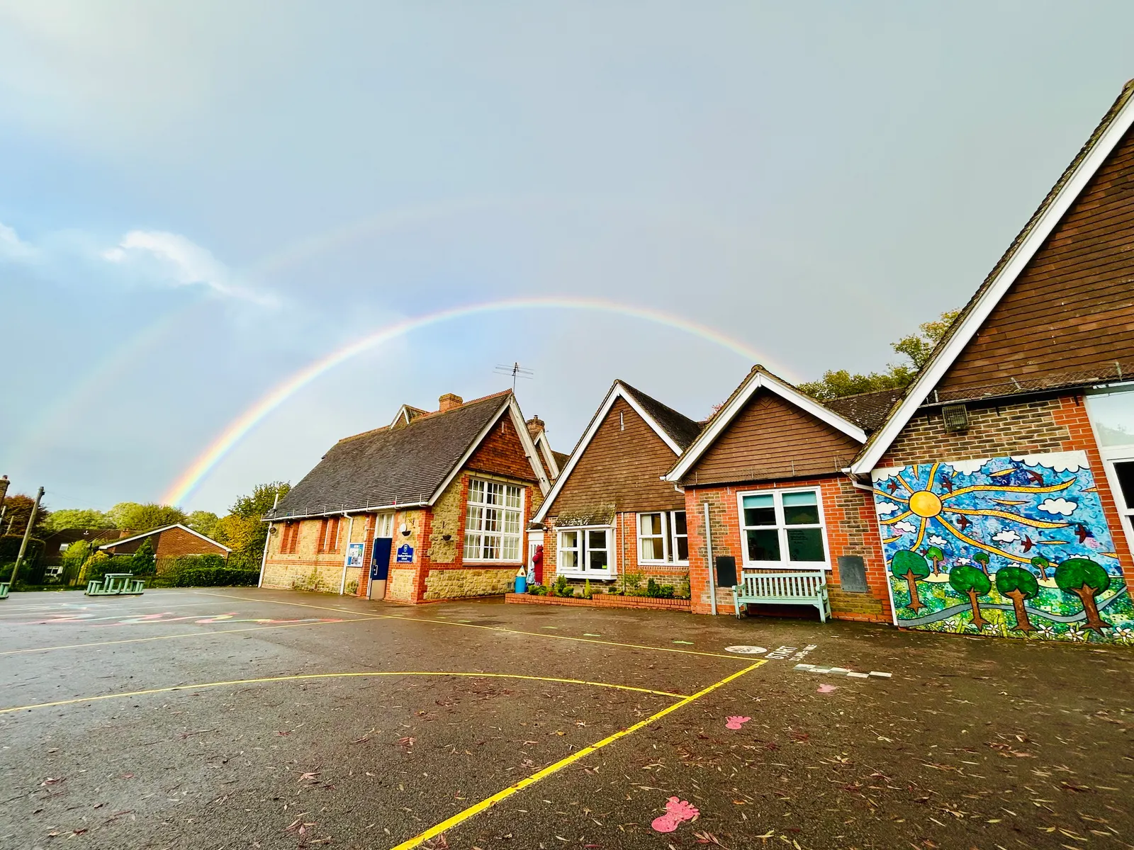A rainbow over the school buildings and the sun mural after rain